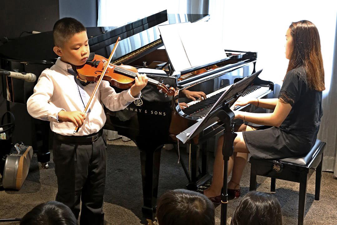 A photo of a boy playing violin and a pianist playing on the piano.