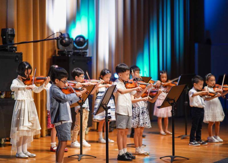 A group of boys and girls performing violin on a wooden stage at a school.